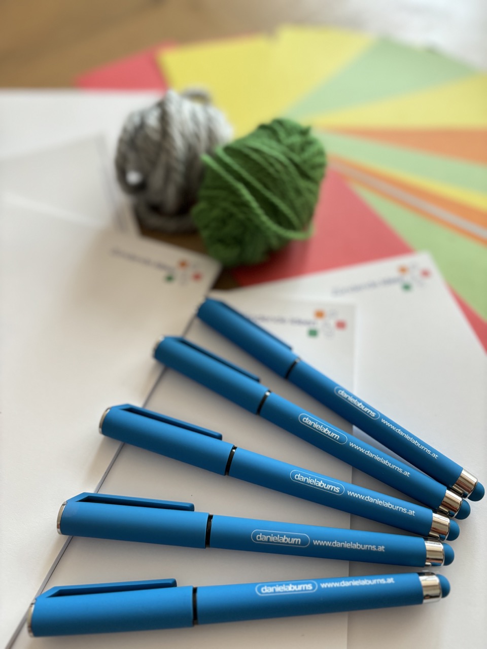 Daniela Burns, Coach in Salzburg, steht mit verschränkten Armen vor einer hellen Wand und lächelt in die Kamera.